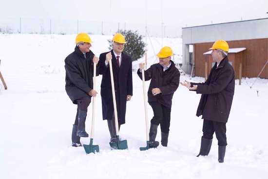4 Männer mit gelbem Bauschutzhelm machen im Schnee den Spatenstich zur Erweiterung des Haus Similasan.