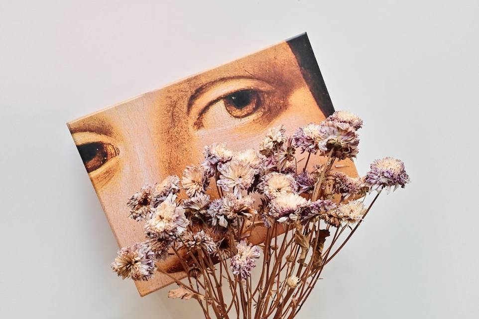 Trockenblumenstrauss darin steckt eine Postkarte mit dem Sujets eines alten Gemäldes mit Augen darauf | ©  Girl with red hat via Unsplash