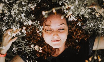 Frau mit lockigem roten Haar liegt in Blumenwiese | © Rodolfo Sanches Carvalho via Unsplash