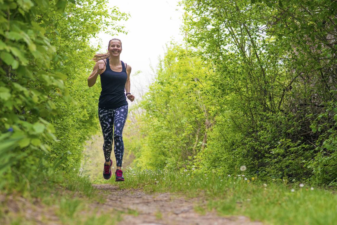 Eine Frau rennt durch den grünen Wald. Homöopathie kann bei Heuschnupfen unterstützen. | © iStock