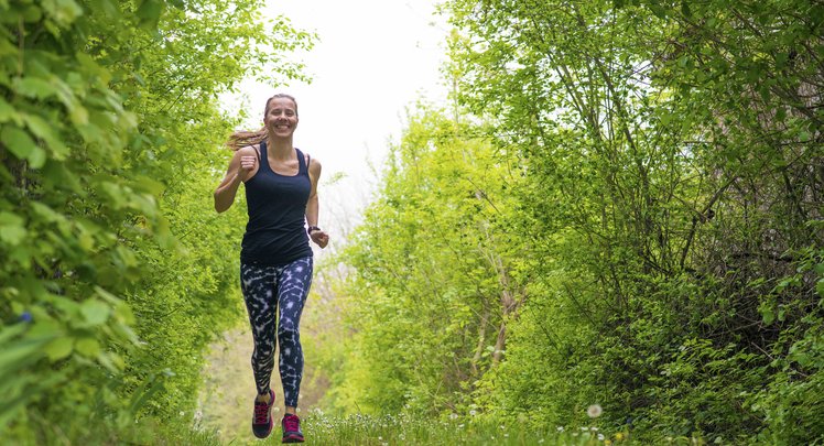 Eine Frau rennt durch den grünen Wald. Homöopathie kann bei Heuschnupfen unterstützen. | © iStock