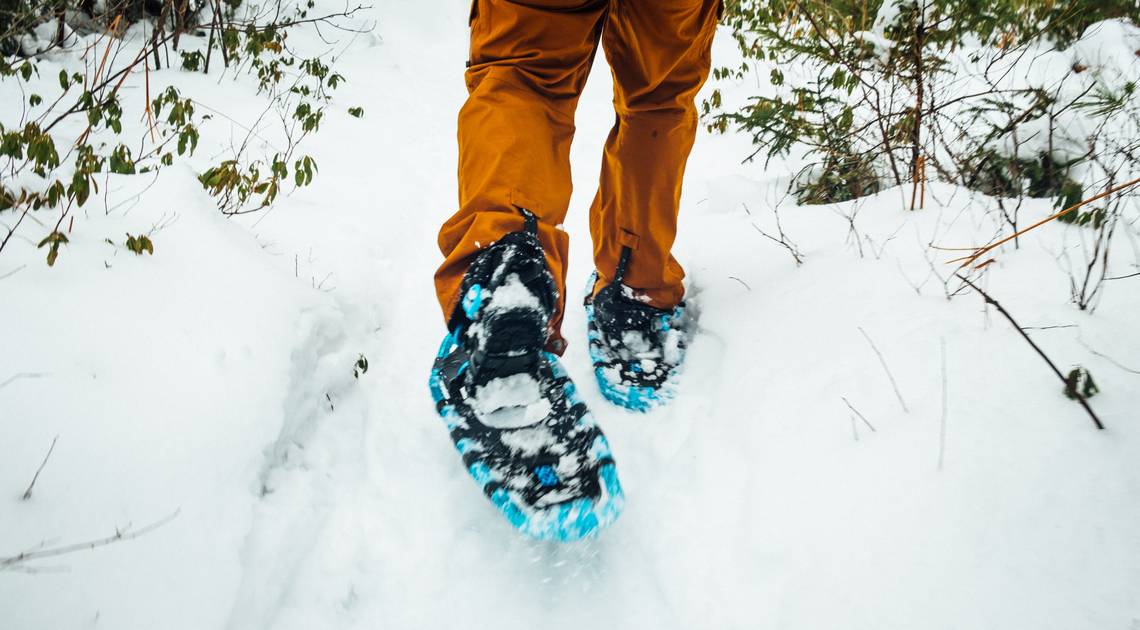 Beine mit orangen Skihosen die in Schneeschuhen durch den weissen Schnee laufen. | © Tim Foster_via Unsplash