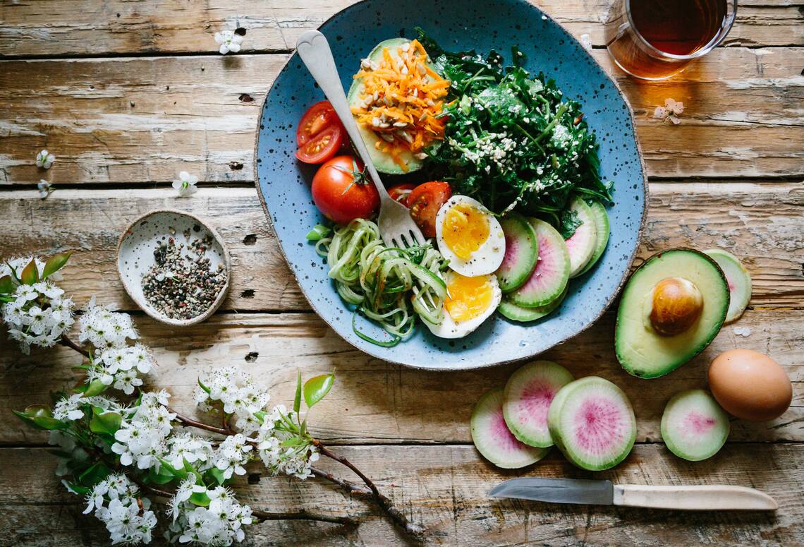 Holztisch mit dem Salatteller drauf mit Spinat, Avocado, Tomate und hartgekochten Eiern. | © Brooke Lark via Unsplash