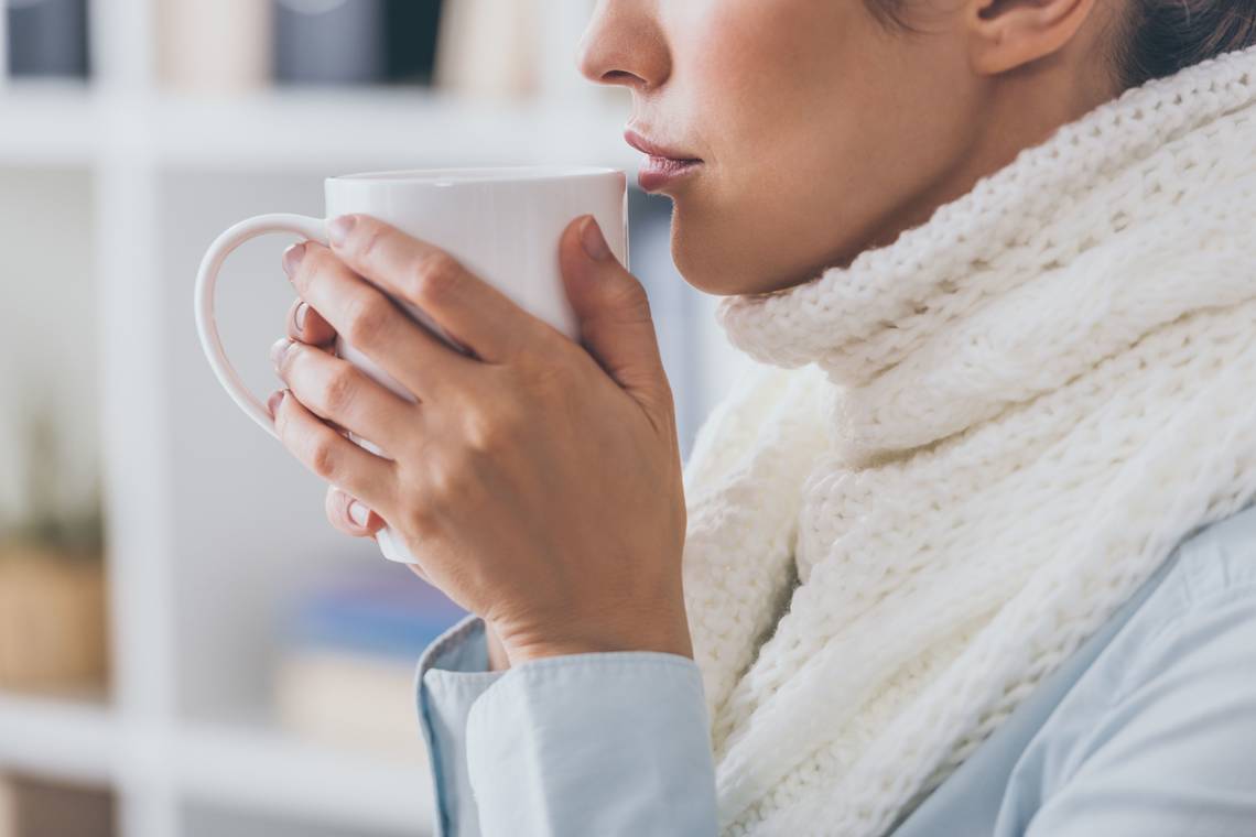 Person mit Schal hält eine warme Teetasse. | © Adobe Stock