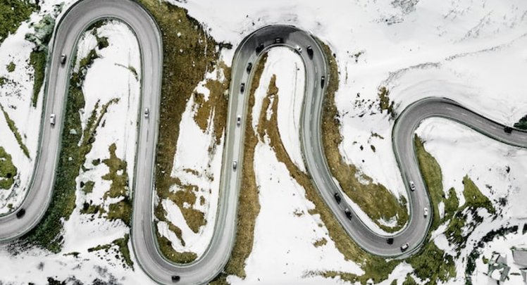 Kurvige Bergstrasse um die Schnee liegt aus der Vogelperspektive | © Markus Gempeler via Unsplash