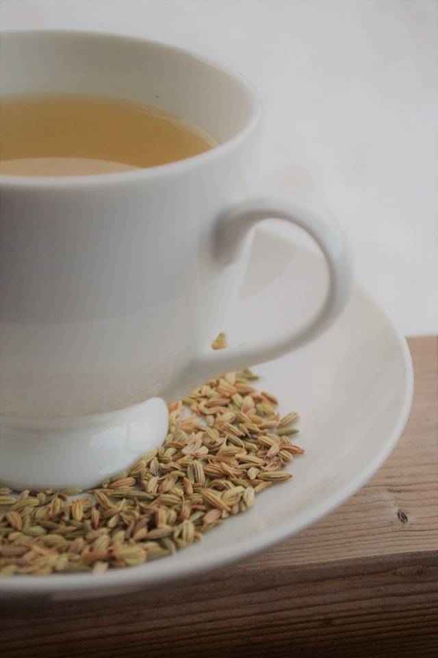 Weisse Teetasse mit Fencheltee drin und Fenchelsamen auf dem Unterteller. | © Jenn Simpson via Unsplash